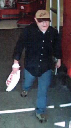 Man exiting target dressed in tan and brown rimmed baseball cap, black dress shirt, jeans and green lace up shoes. 